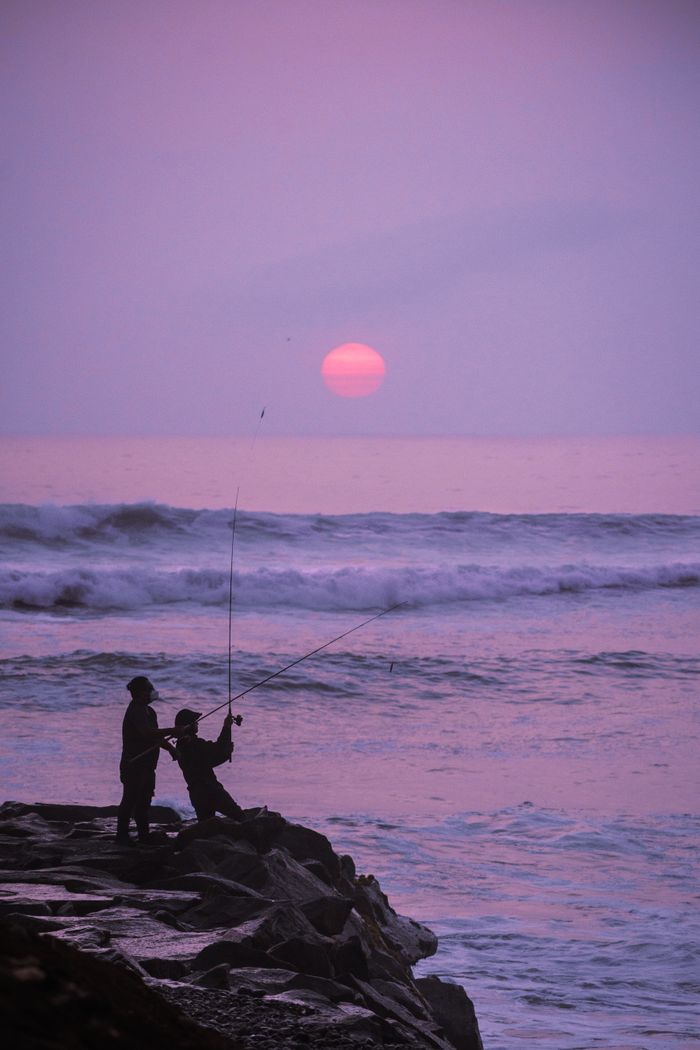 Silhouetted fishermen casting lines at sunset on Callao Beach in Peru, capturing a tranquil seascape.